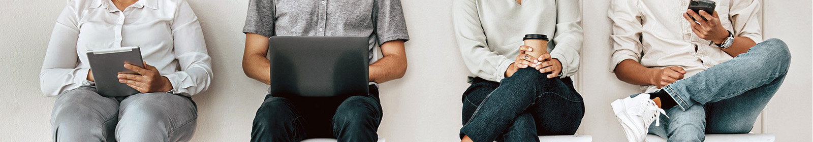 Four people sitting in chairs with a tablet, a laptop, coffee and a mobile phone